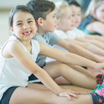  Elementary students sitting on a gym floor exercising